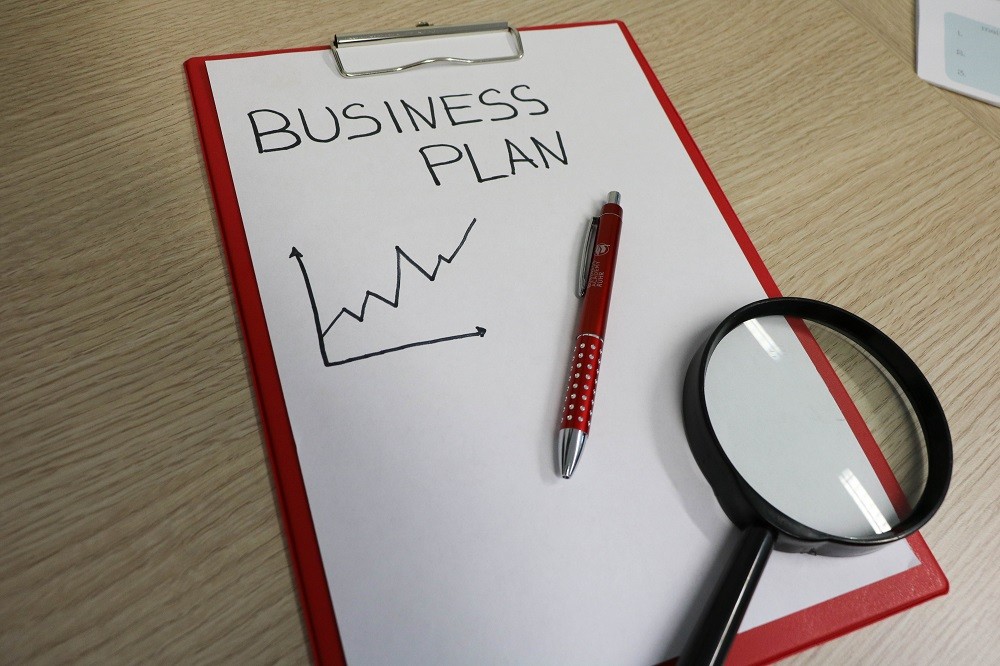 Weißes Papier auf einem roten Klemmbrett mit der Aufschrift "Business Plan"