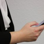 Frau mit schwarzen Blazer und weißer Bluse tippt auf ihrem Smartphone