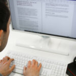 Mann sitzt an PC und tippt auf Tastatur