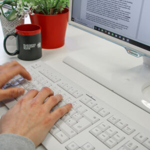 Mann tippt auf einer weißen Tastertur einen Text auf den Bildschirm